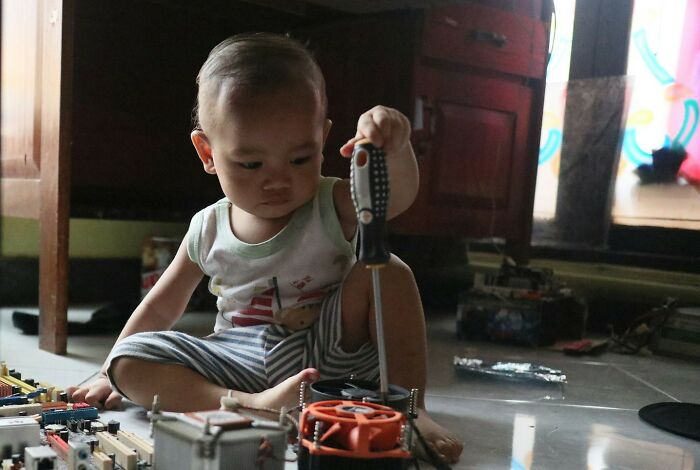 Toddler exploring electronics with a screwdriver, showing surprising intelligence and curiosity in a home setting.