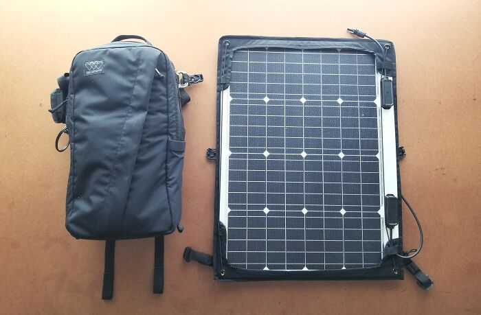 Black backpack and portable solar panel laid out on a table symbolizing progress and hope in America.