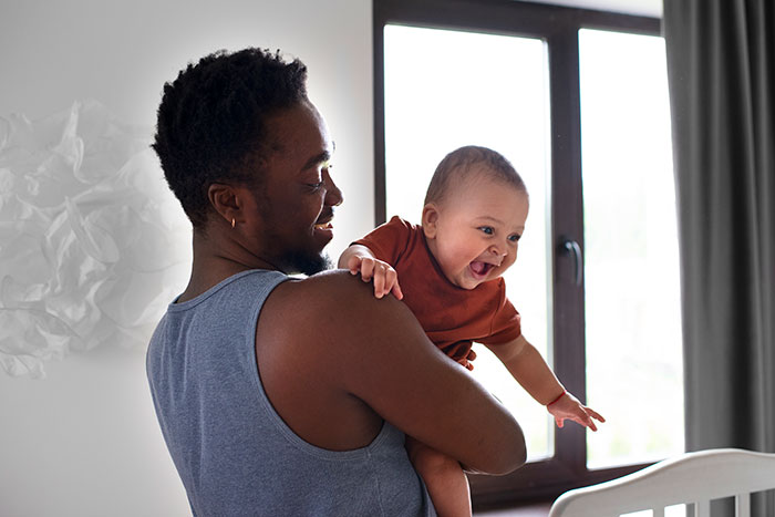 Father holding newborn baby indoors, capturing a very Jerry Springer moment of babies looking nothing like their father.