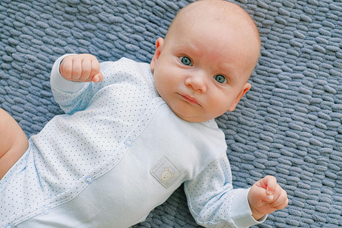Newborn baby lying on a textured blue blanket looking confused, illustrating newborns who look nothing like the father.