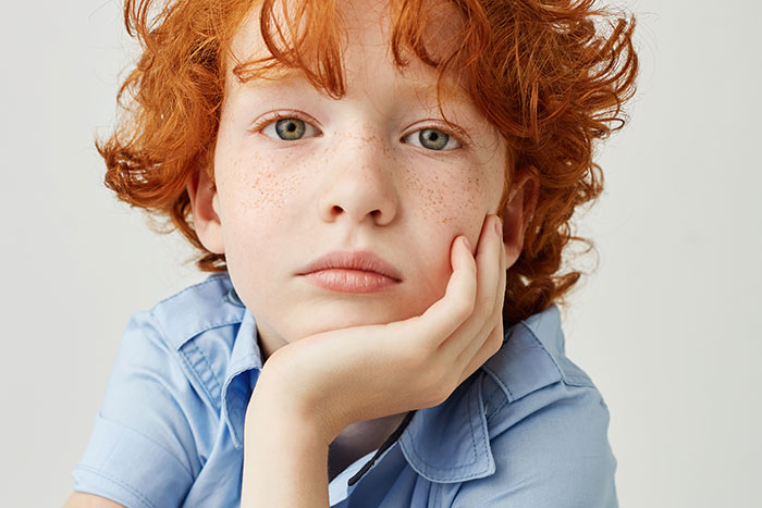 Redheaded boy with freckles and green eyes, looking thoughtful and unrelated to father, illustrating newborn confusion.