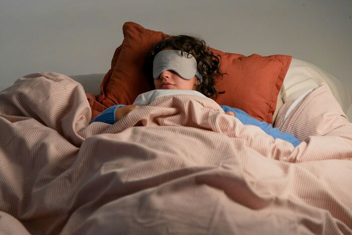 Person asleep with eye mask in cozy bed, soft pillows and blankets, illustrating creepiest displays of intelligence.