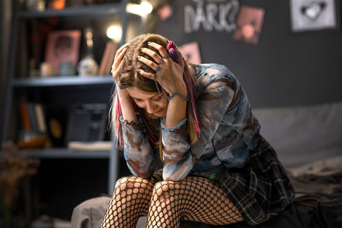 Young adult worker daughter sitting distressed in bedroom after parents disown and insult her fiancé years ago. Young adult worker daughter sitting distressed in bedroom after parents disown and insult her fiancé years ago.