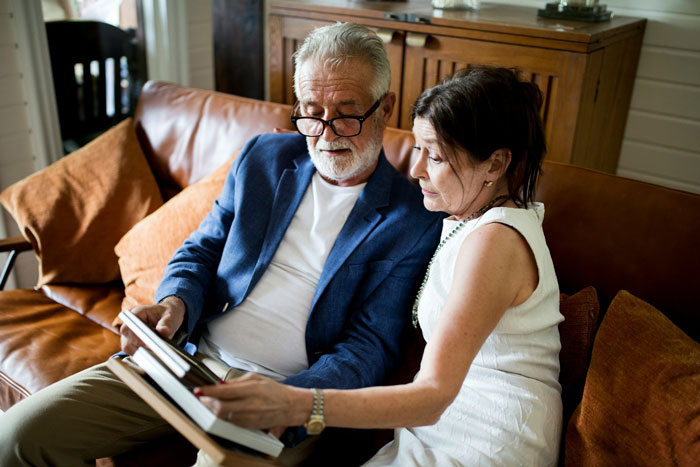 Older couple discussing family matters on a couch, illustrating tension around parents pressuring about having kids and inheritance threats.
