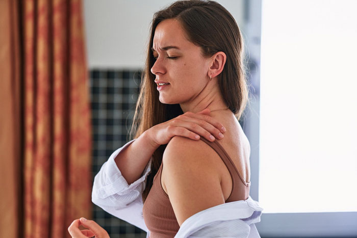 Woman holding her shoulder in pain at home, illustrating partner sleep called ambulance myself situation.