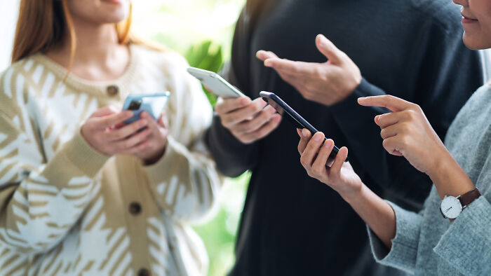 Three people using smartphones and discussing real-life cheat codes in a casual indoor setting.