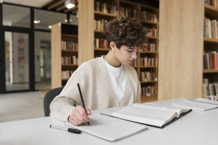 Person studying and writing notes in a library, using real-life cheat codes to improve learning efficiency and retention.