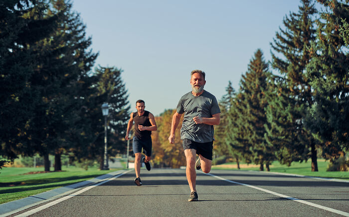 Two men running on a tree-lined road outdoors using real-life cheat codes for fitness and endurance improvement.