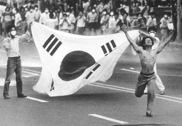 Protester running with South Korean flag during a historic moment, capturing powerful emotions from their country.