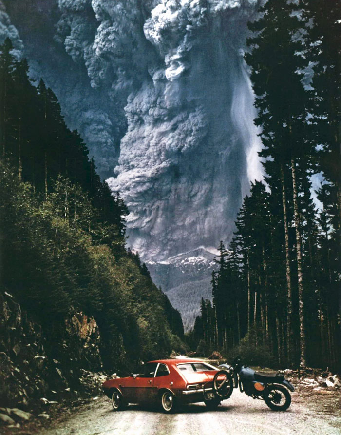 Red car and motorcycle on a forest road with a massive erupting volcano in the background, a powerful country photo that hits hard.