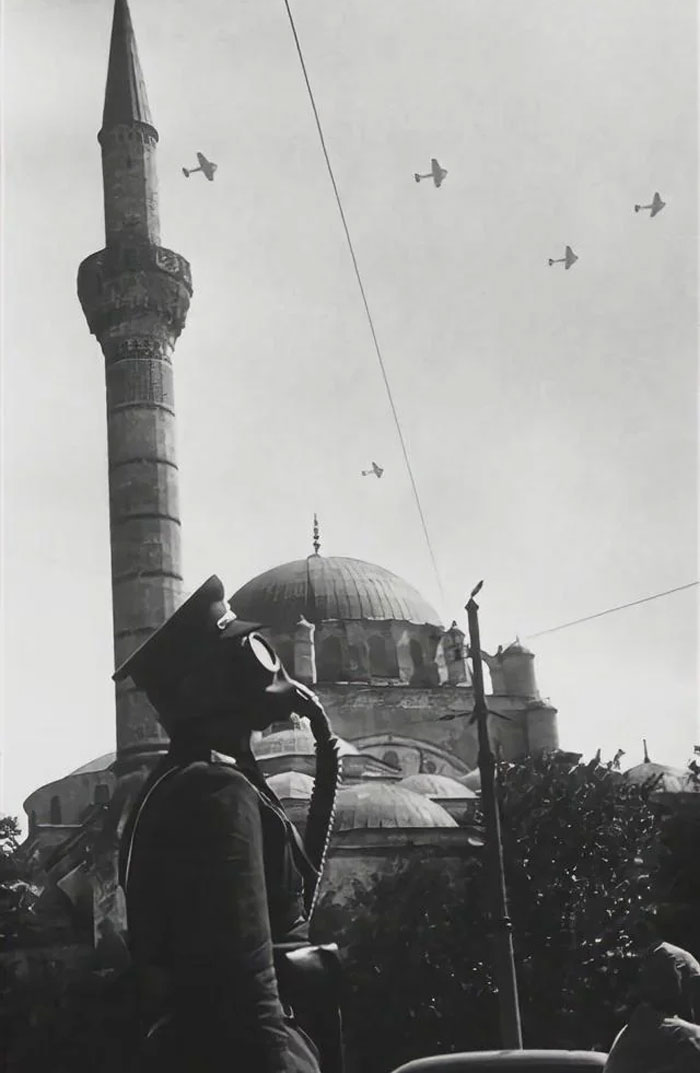 Person wearing a gas mask near a mosque with airplanes flying overhead in a powerful photo from their country that hit hard.