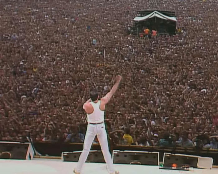 Performer in white outfit on stage facing a massive crowd of fans captured in a powerful country photo that hits hard.