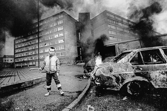 Child standing near a burning car in a devastated urban area, a powerful photo from impactful country moments shared.