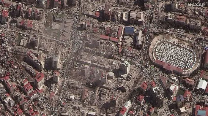 Aerial view of widespread destruction in a city showing damaged buildings and emergency tents in a country.