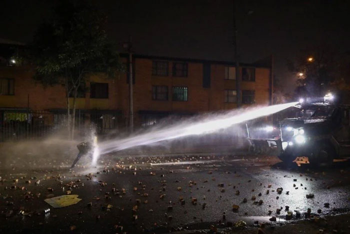 Protester hit by water cannon during nighttime street clash in a country scene that always stayed with me.