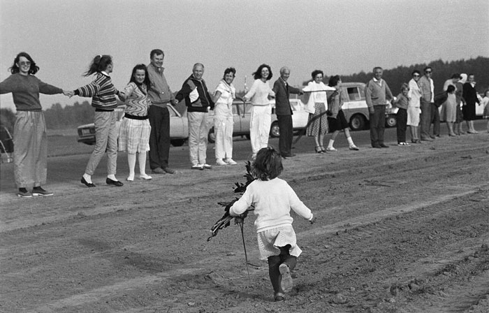 Child holding flowers running towards a group of people holding hands in a country photo that hits hard.
