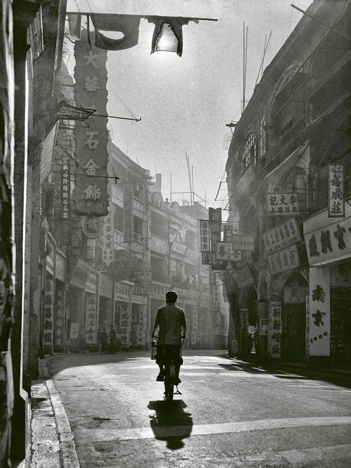 Man riding bicycle on empty street lined with vintage signs, a photo from countries that hit hard memories.