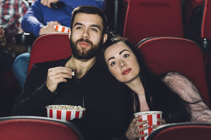 Couple sharing popcorn and watching a movie in a theater, illustrating people sharing wildest ways found out cheating.