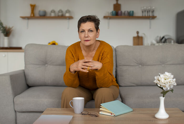 Woman in an orange sweater sitting on a gray couch, sharing stories about the worst person they've ever met.