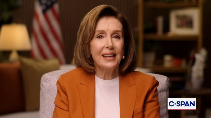 Woman speaking in a warmly lit room with an American flag in the background, sharing stories about the worst person they've met