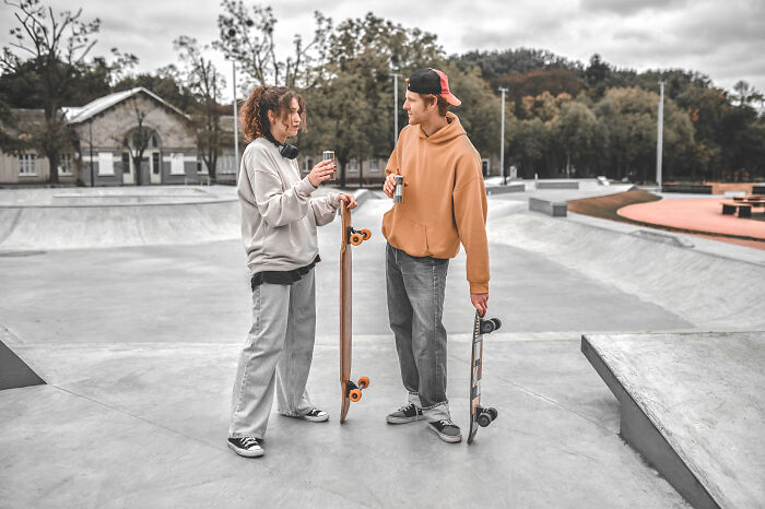 Two young people at skate park sharing stories about the worst person they've ever met, each holding a skateboard.