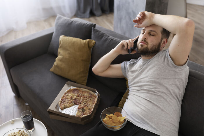 Man looking distressed on phone while lounging with pizza and chips, illustrating stories about the worst person they've met.