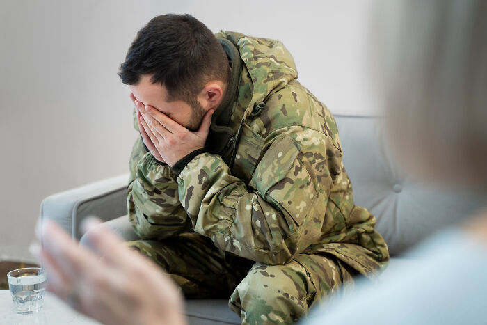Worried soldier in camouflage covering his face on a sofa during a Moments People Faced support session
