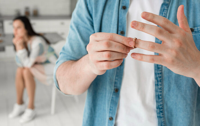Person removing wedding ring with upset partner sitting in the background, illustrating strange tales of folks who morphed.
