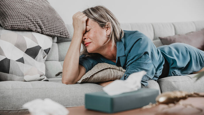 Woman lying on couch with eyes closed and hand on forehead, depicting struggle in strange tales of folks who morphed