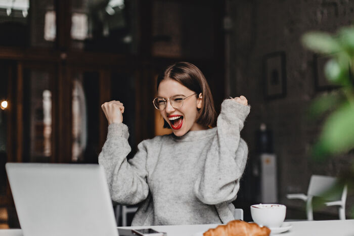 Young woman excitedly celebrating success while using laptop, illustrating strange tales of folks who morphed unexpectedly.