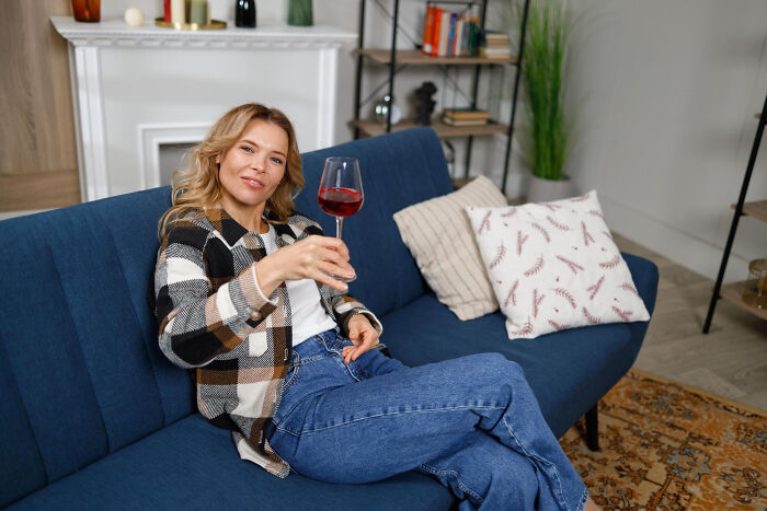 Woman relaxing on a blue sofa holding a glass of wine, illustrating strange tales of folks who morphed unexpectedly.