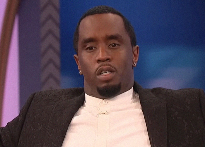 Man in a dark blazer and white shirt speaking in a TV interview about celebrity passings that surprised fans.