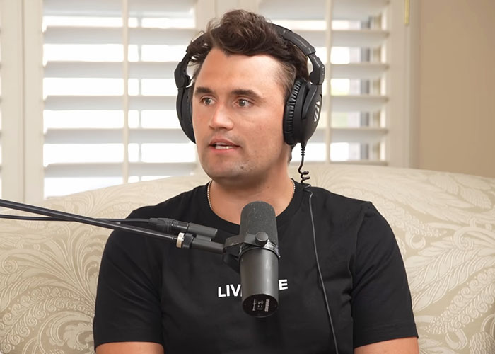 Man wearing headphones and a black shirt speaking into a microphone during a podcast about celebrity passings.
