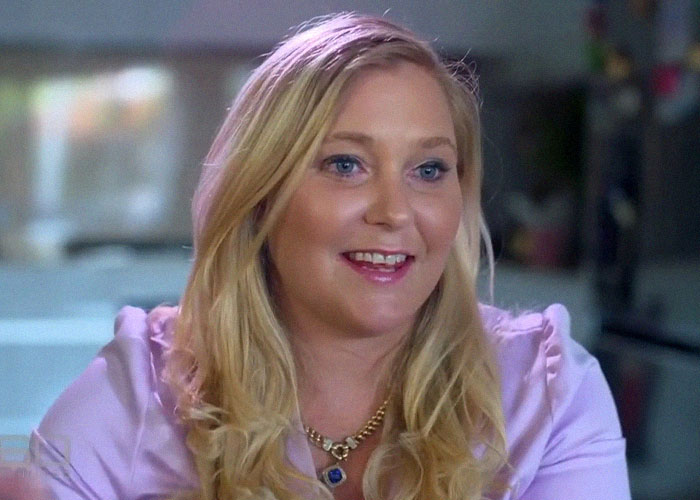 Blonde woman wearing a purple blouse and a gold necklace, smiling during a casual interview about celebrity passings.