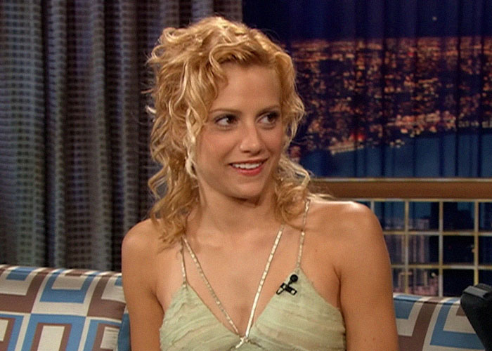 Actress with curly blonde hair smiling during a late night talk show interview about celebrity passings.
