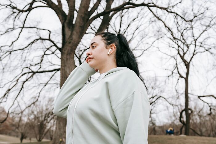Young woman wearing earbuds and a hoodie standing outdoors among bare trees, reflecting on things that shocked people after prison.