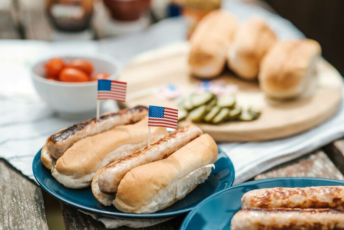 Grilled hot dogs in buns with small American flags, symbolizing uplifting stories of progress and hope in America.