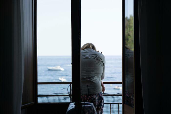 Person leaning on balcony railing looking at boats on the sea, illustrating cheat codes for everyday life easier.