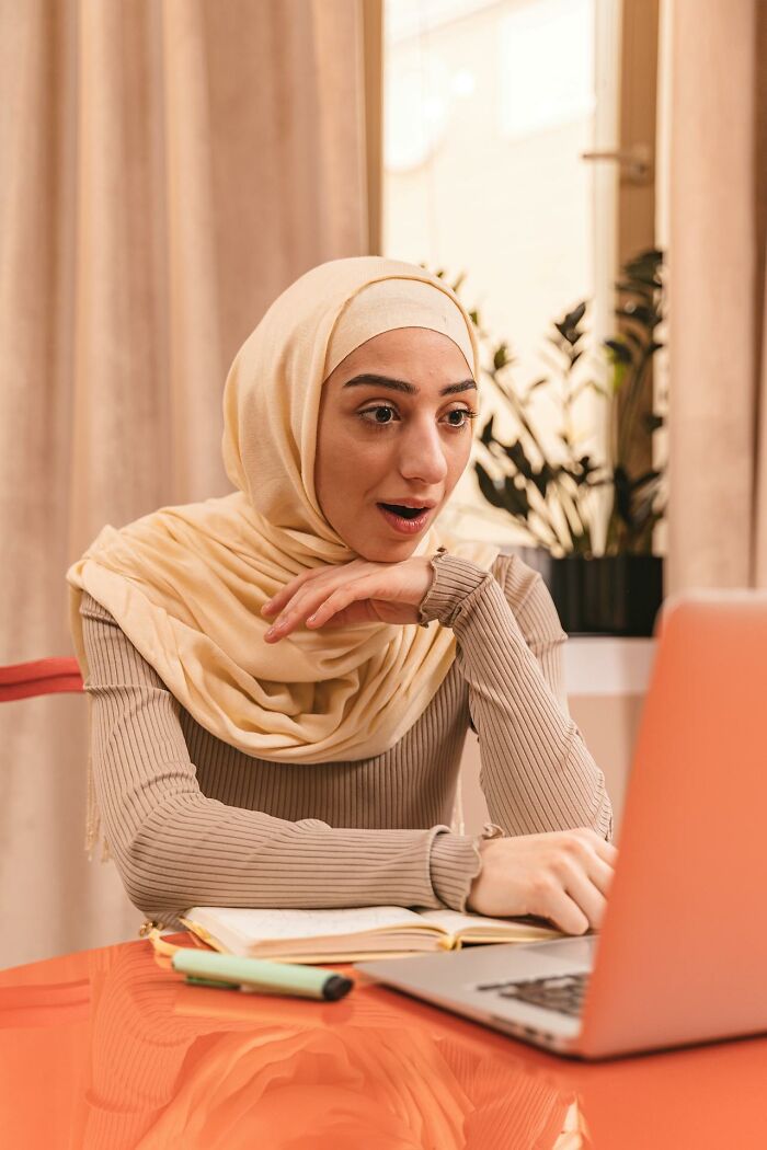 Surprised woman wearing headscarf at laptop reacting to a wild rained frogs anecdote