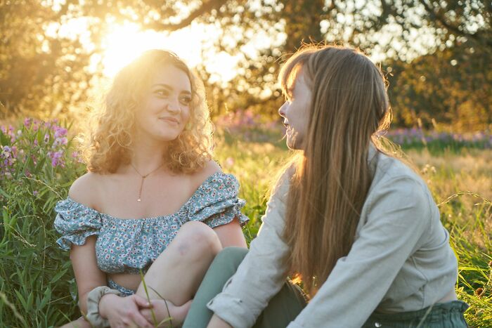 Two women sitting in a sunny field, smiling and talking, illustrating everyday life cheat codes for easier living.