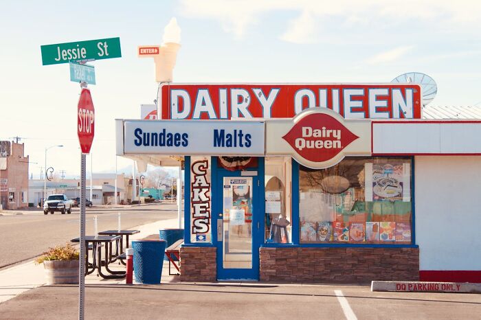 Dairy Queen storefront on a quiet street corner with signs for sundaes, malts, and cakes in public.