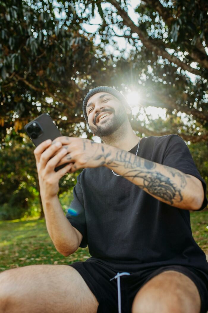 Man with tattoos smiling while looking at phone outdoors, capturing accidental texts causing panic moments.