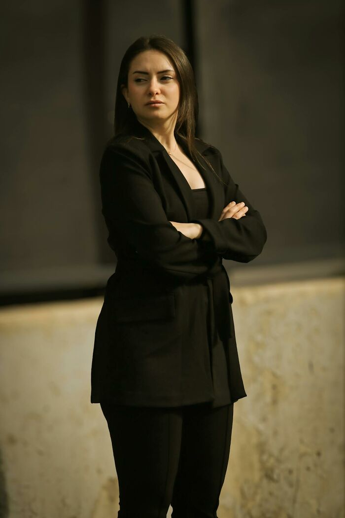 Woman in black suit standing with arms crossed, representing rich people detached from reality concept.