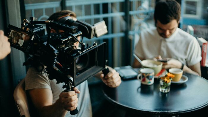 Filmmaker operating a professional camera in a cafe setting capturing scenes for films that got lost in translation. Filmmaker operating a professional camera in a cafe setting capturing scenes for films that got lost in translation.