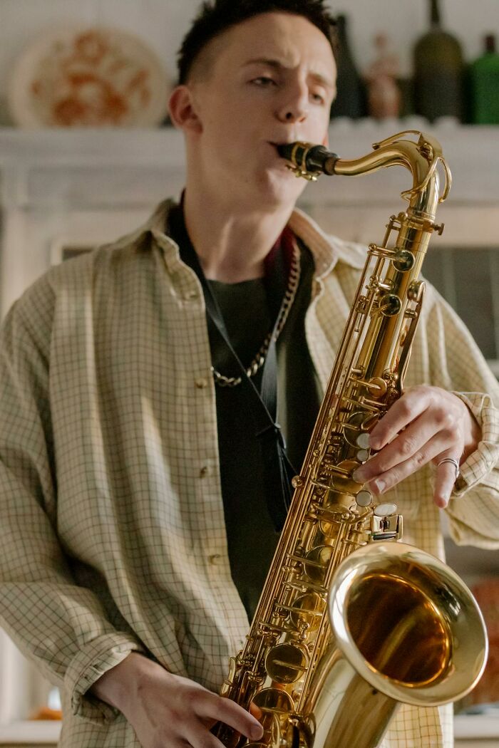 Young man playing saxophone indoors in plaid shirt, candid portrait, creepiest displays of intelligence