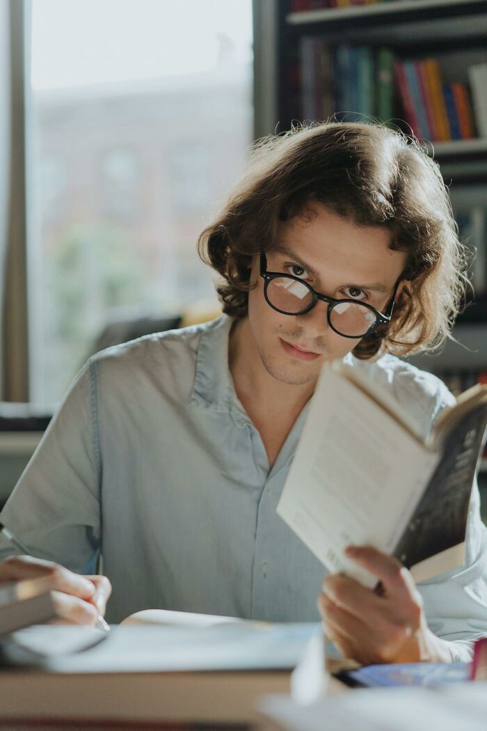 Young man with glasses reading in a library, intense stare; creepiest displays of intelligence