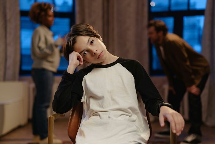 Teen boy looking thoughtful while two adults argue in the background, illustrating family secrets tension.