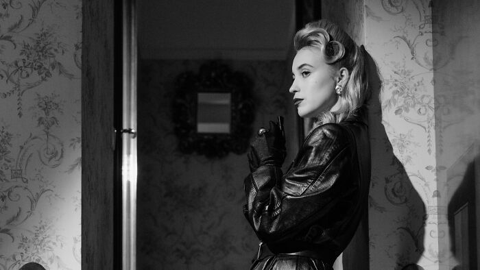 Black and white image of a side character in a leather jacket posing dramatically indoors for films and TV shows.