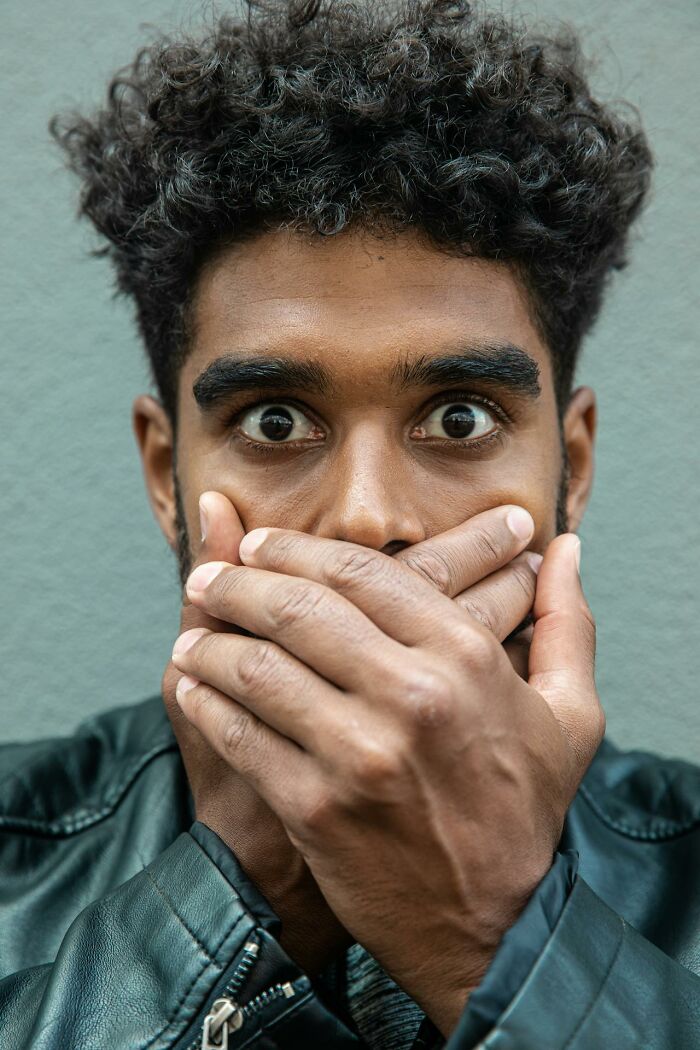 Close-up of a night shift worker covering his mouth with hands, showing shock and chaos during a 3 AM work moment.