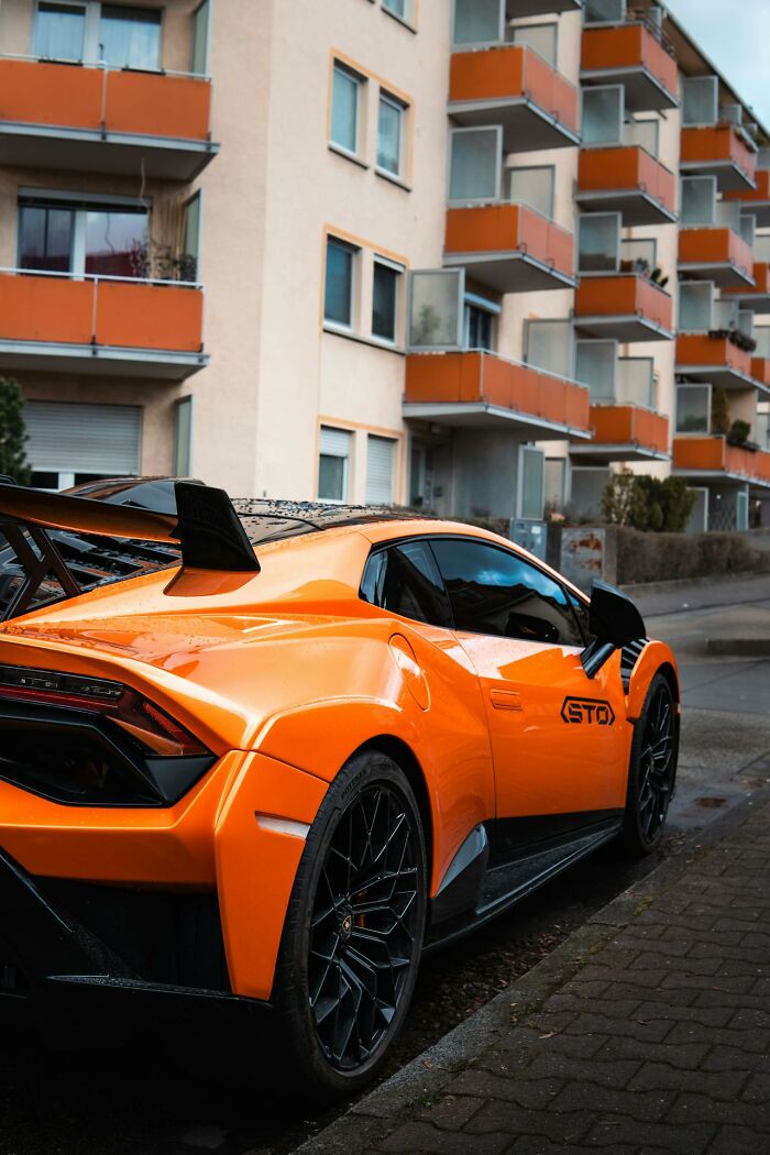 Orange luxury sports car parked on a city street highlighting how rich people show how far from reality they are.